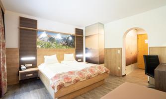 A modern hotel room with two beds and wood-colored furniture. In the background, there is a wall with mountain motifs.