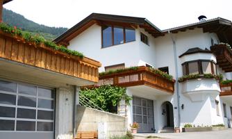 A modern house with wooden siding and large windows. It is located in a mountainous area.