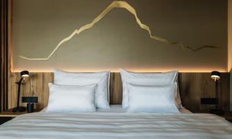 A modern bedroom with a large bed and two nightstands. On the wall is a stylized mountain silhouette in golden color.
