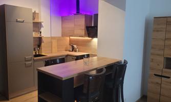 A modern kitchen with wooden cabinets and a small bar. The lighting is in a calming shade of violet.