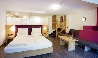 A modern room with a double bed, wooden details, and a cozy seating area. The decor is bright and inviting, perfect for relaxation.