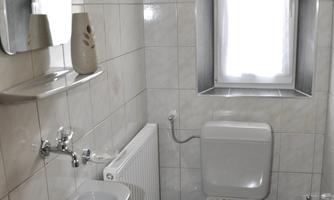 A small bathroom with bright tiles and a window. On the floor is a red towel, and there is a toilet and a sink visible.