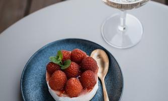 A delicious strawberry cake on a blue plate with a wooden spoon. Next to it is a glass of sparkling drink.