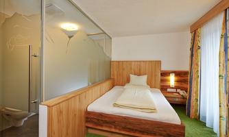 A modern bedroom with wooden paneling and a large bed. The large window front provides plenty of daylight.