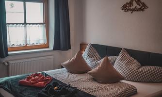 A cozy bedroom with a large bed and beige pillows. The windows let in plenty of light and the wall decoration features the mountains.