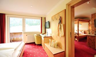 A cozy hotel room with a red carpet and a large window. On the right, you can see a separate sleeping nook in a rustic style.