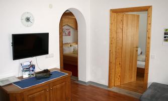 A cozy room with a television and a wooden desk. In the background, a door to a sleeping area is visible.