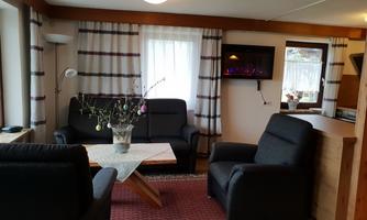 A cozy living space with two black sofas and a coffee table. Large windows let in a lot of light, and there is a decorative plant in the middle.
