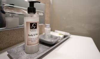 An elegant soap dispenser for body and hair stands on a modern shelf. Next to it, other small care products are placed.