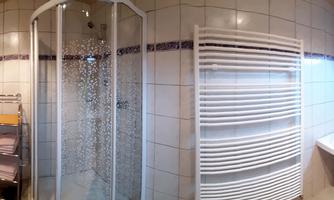 A modern bathroom with a shower, toilet, and sink. The walls are tiled and there are towels on a rack.