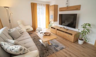A modern living room with an inviting sofa and a wooden coffee table. Large windows let in plenty of light and a plant provides a fresh accent.