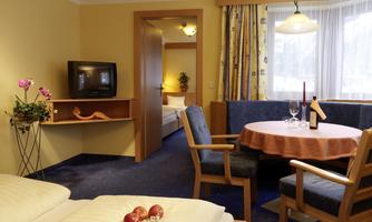 A cozy room with a double bed and a seating area. The room has bright walls and large windows that provide plenty of light.