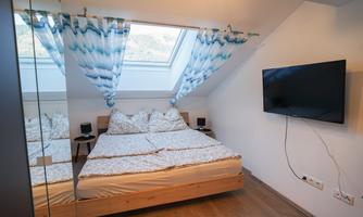 A modern bedroom with a large window and bright curtains. The bed is made of wood and the walls are simply designed.