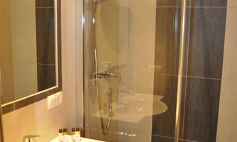 A modern bathroom with a glass shower and a sink. The walls are elegantly tiled and well-lit.