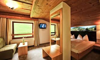A cozy room with wooden elements, a large window, and a beautiful view. There is a double bed, a small table, and a television.