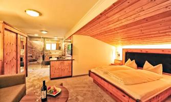 A cozy hotel room with wooden paneling and a large bed. There is a small table with wine and fruit as well as a television in the background.