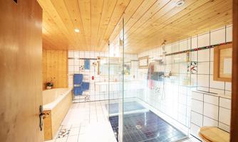 A modern bathroom with a wood ceiling and tiled walls. There is a shower cabin, a tub, and plenty of space for personal care.