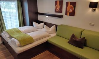 A modern room with a double bed and a green seating area. Large windows provide plenty of daylight.