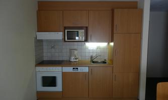 A modern wooden kitchen with a stove, a microwave, and a small sink. The kitchen unit is functional and well-organized.