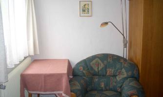 A small room with a comfortable armchair, a table, and a floor lamp. A framed picture hangs on the wall.