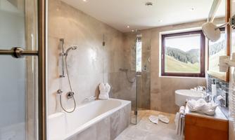 A modern bathroom with a bathtub and a separate shower. The large window offers a view of the green landscape outside.