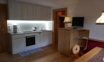 A modern kitchen with bright furniture and a fine wood surface. In the background, a television and a table can be seen.