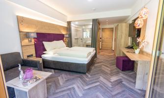 A modern hotel room with wood paneling and a large bed. The decor is stylish and cozy, perfect for relaxing.