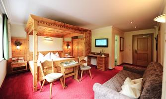 A cozy hotel room with wooden paneling and a large bed. The room features a dining area and a sofa, perfect for relaxation.