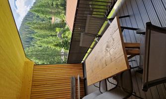 A cozy balcony with a wooden table and chairs. In the background, green trees and hills are visible.