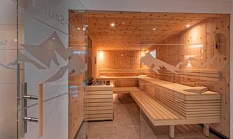 A modern sauna room with wooden paneling and pleasant lighting. The glass door allows a view of the inviting atmosphere.