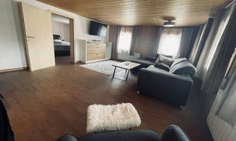 A cozy living room with wooden floors and large windows. There is a couch, a coffee table, and modern furniture.