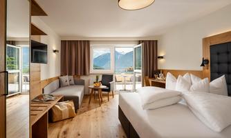 A modern hotel room with a large bed and a cozy seating area. Large windows provide a view of the mountains.