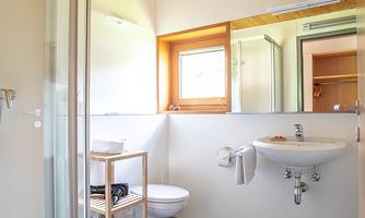 A modern bathroom with shower, sink, and wooden ceiling. It is bright and cheerfully furnished.