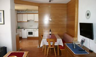A modern kitchen with a dining area, wooden paneling, and a cozy table. The space is designed to be bright and welcoming.