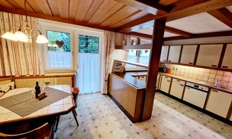A cozy kitchen with wooden paneling and a dining area. Large windows provide plenty of light and a view of the outdoors.