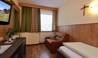A cozy hotel room with wooden floors and warm colors. There is a sofa, a television, and large windows with curtains.