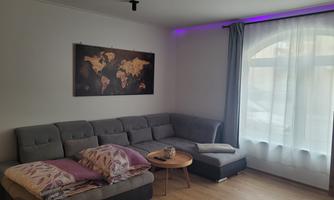 A modern living room with a gray couch and a round table. A world map hangs on the wall and the window is decorated with a light curtain.