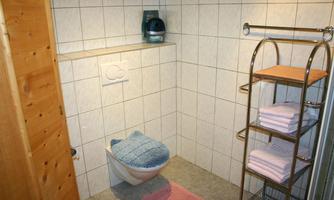 A clean bathroom with a toilet and a towel rack. There are folded towels and a small rug on the floor.