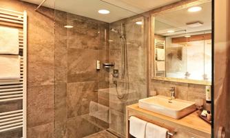 A modern bathroom with a glass shower and an elegant sink. The walls are adorned with gray tiles, and there are fresh towels.