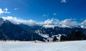 A snow-covered mountain landscape under a clear blue sky. In the foreground, ski tracks and an observation point are visible.