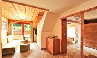 A cozy room with wooden paneling and large windows. The furnishings include a sofa, a small table, and a wooden wardrobe.