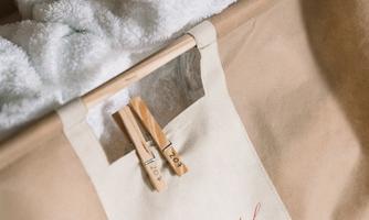 A laundry basket with freshly washed towels that are neatly folded. The basket has an etched logo and two wooden clips.
