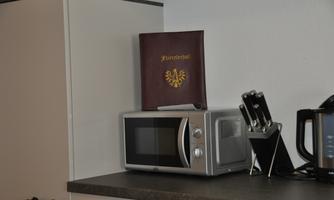 A modern microwave is on a kitchen countertop. Next to it is a red book with a golden crest.