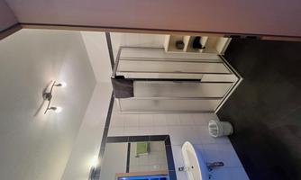A modern bathroom with a shower, a sink, and a small shelf. The walls are brightly tiled and the floor is dark.