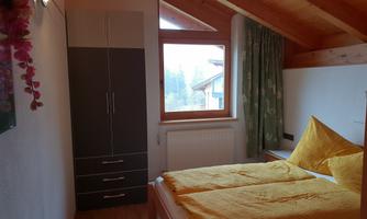A cozy bedroom with a double bed and yellow pillows. The windows offer a view of the outside and the room has wooden details.