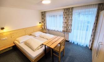 A simple bedroom with two single beds and a table.  
Large windows let in plenty of daylight.