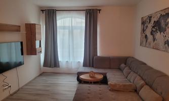 A modern living room with a gray sofa and a round table. A large window with curtains provides plenty of natural light.