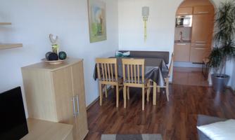 A bright apartment with a dining area and modern furnishings. In the background, the kitchen is visible, which conveys a cozy atmosphere.
