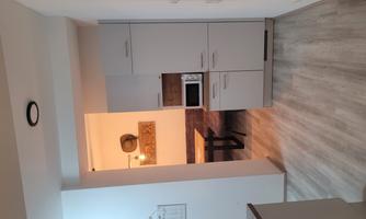 A modern kitchen with white cabinets and a microwave. In the background, a dining area with a table and benches is visible.