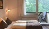 A cozy bedroom with a double bed and bright light. The window offers a view of nature and a small balcony.